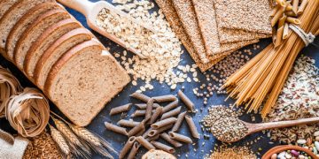 Whole grain foods including bread, oats, pasta, and seeds spread on a table, beneficial for constipation treatment.