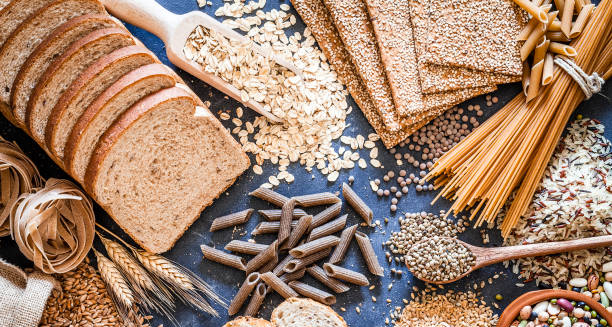 Whole grain foods including bread, oats, pasta, and seeds spread on a table, beneficial for constipation treatment.