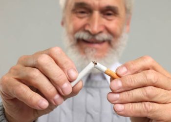 Smiling elderly man breaking a cigarette in half, symbolising smoking cessation as part of coronary heart disease treatment.