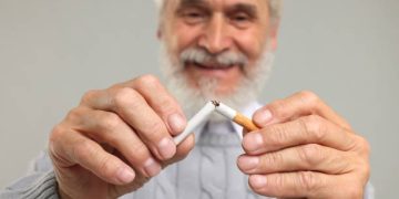 Smiling elderly man breaking a cigarette in half, symbolising smoking cessation as part of coronary heart disease treatment.