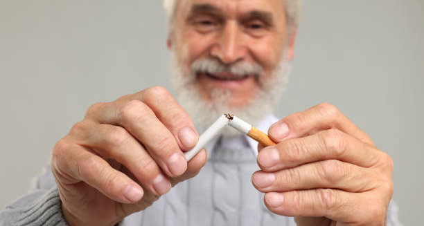 Smiling elderly man breaking a cigarette in half, symbolising smoking cessation as part of coronary heart disease treatment.