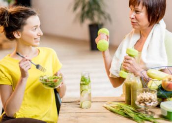 Two women discussing health while enjoying a salad and green smoothies, representing lifestyle and dietary management in treating Crohn’s disease.