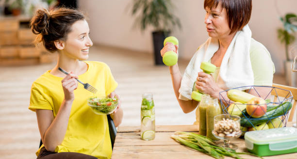 Two women discussing health while enjoying a salad and green smoothies, representing lifestyle and dietary management in treating Crohn’s disease.