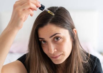 Woman applying hair serum with dropper to treat dandruff