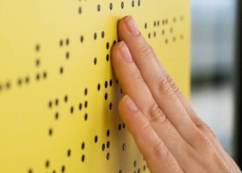 Hand reading Braille on a yellow board