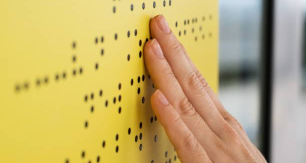 Hand reading Braille on a yellow board