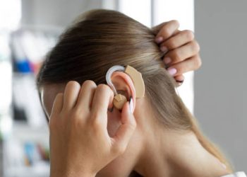 Woman adjusting a modern hearing aid behind her ear