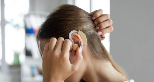 Woman adjusting a modern hearing aid behind her ear