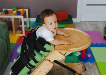 Toddler receiving physical therapy in a standing support chair for hip dysplasia