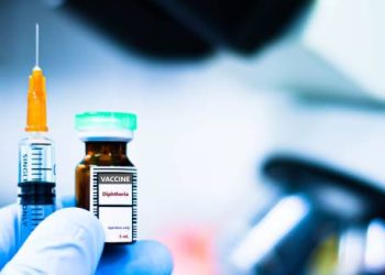 Diphtheria vaccine bottle and syringe held by a gloved hand