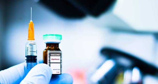 Diphtheria vaccine bottle and syringe held by a gloved hand