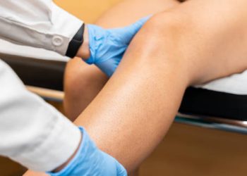 Doctor examining patient’s knee for dislocation treatment on clinic bed