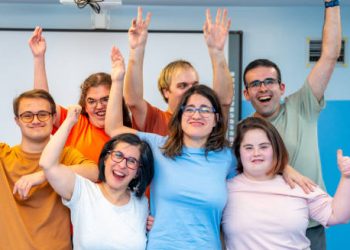 Group of young adults with Down’s syndrome smiling and raising their hands in a cheerful environment