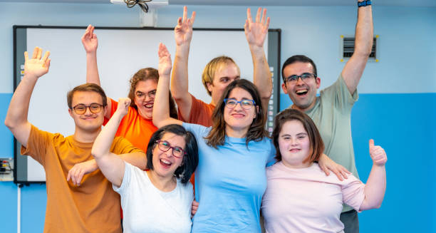 Group of young adults with Down’s syndrome smiling and raising their hands in a cheerful environment
