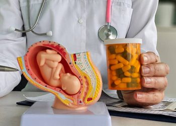 Doctor explaining treatment of ectopic pregnancy with pregnancy model and medication bottle.