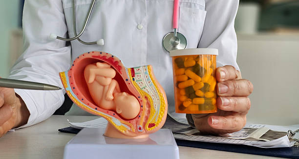 Doctor explaining treatment of ectopic pregnancy with pregnancy model and medication bottle.