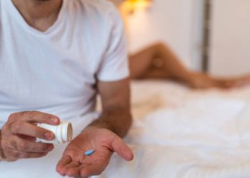 Man sitting on bed taking a blue pill for erectile dysfunction treatment