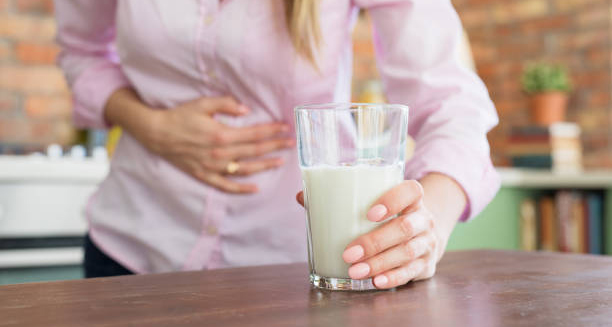 Woman holding her stomach and placing a glass of milk on a table, indicating lactose intolerance