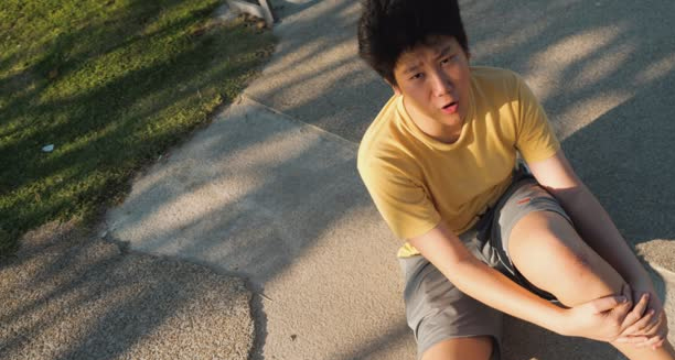 Teen boy sitting on pavement after falling and grazing his knee