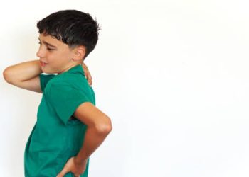Boy showing signs of growing pains by holding his back and shoulder