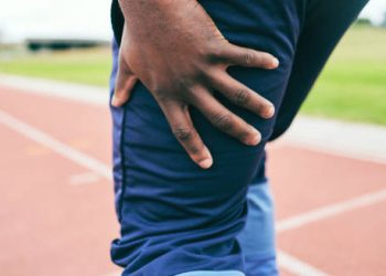 Athlete holding the back of his thigh in pain after a hamstring strain on the track
