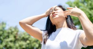Woman wiping her forehead under intense sun, showing signs of overheating