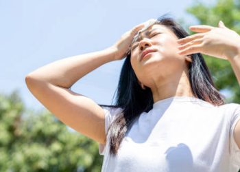 Woman wiping her forehead under intense sun, showing signs of overheating
