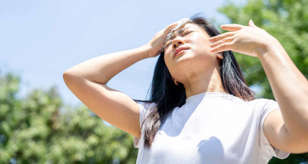Woman wiping her forehead under intense sun, showing signs of overheating