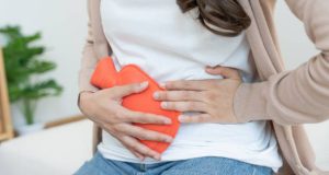 Woman holding hot water bottle to abdomen during heavy menstrual bleeding