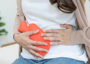 Woman holding hot water bottle to abdomen during heavy menstrual bleeding