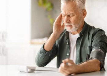 Elderly man experiencing dizziness while checking blood pressure at home