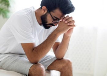 Frustrated man sitting on bed with head in hands, struggling with impotence