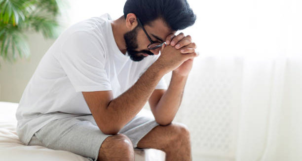 Frustrated man sitting on bed with head in hands, struggling with impotence