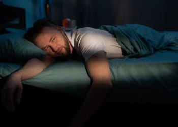 Tired man lying awake in bed at night with a fatigued expression