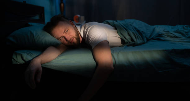 Tired man lying awake in bed at night with a fatigued expression