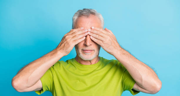 Elderly man covering his eyes with hands on blue background