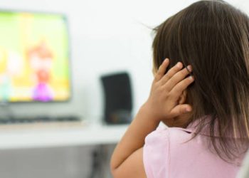 Child covering ears while watching TV, indicating potential hearing issues from glue ear