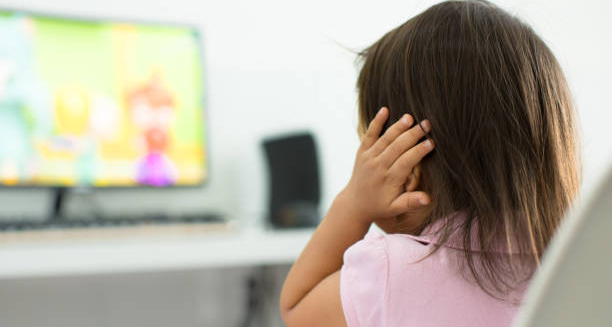 Child covering ears while watching TV, indicating potential hearing issues from glue ear