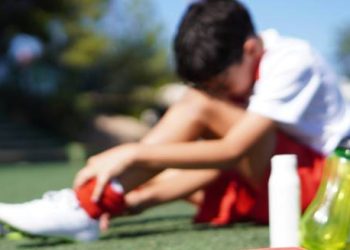 Young athlete sitting on field holding hamstring in pain.