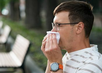 Man sneezing into tissue outdoors, experiencing severe hay fever symptoms