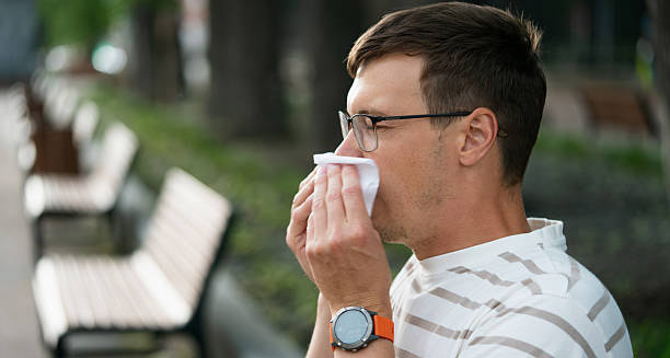 Man sneezing into tissue outdoors, experiencing severe hay fever symptoms