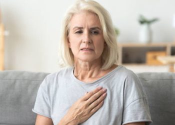 Concerned elderly woman clutching her chest while sitting on a couch
