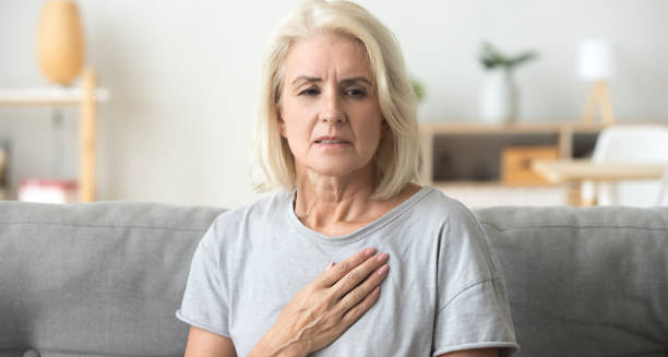 Concerned elderly woman clutching her chest while sitting on a couch