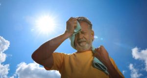 Older man wiping sweat in the sun, showing signs of heat exhaustion complications