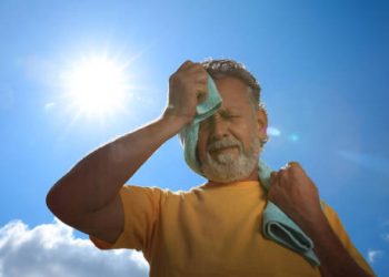 Older man wiping sweat in the sun, showing signs of heat exhaustion complications