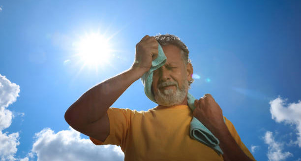 Older man wiping sweat in the sun, showing signs of heat exhaustion complications