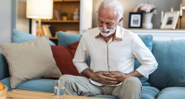 Elderly man experiencing abdominal pain while sitting on a couch