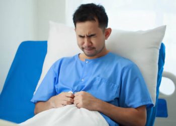 Man in hospital bed clutching stomach in pain due to complications of hiatus hernia