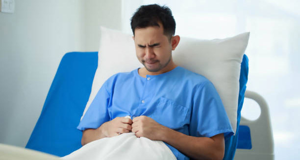 Man in hospital bed clutching stomach in pain due to complications of hiatus hernia