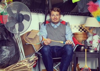 Man surrounded by clutter and household items in a hoarded room